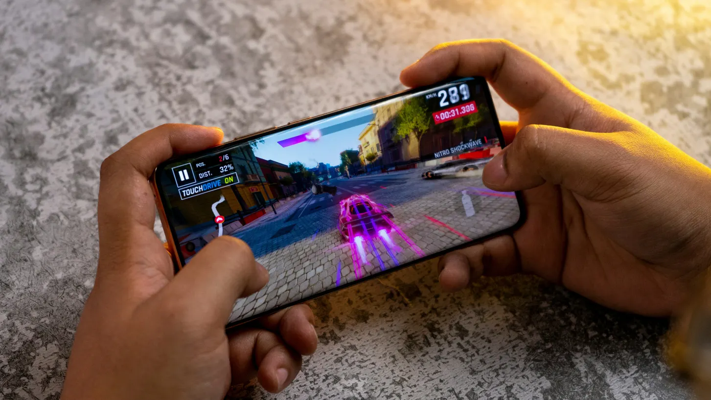 Player holding a smartphone while playing a mobile racing game, illustrating repeat mobile game engagement.